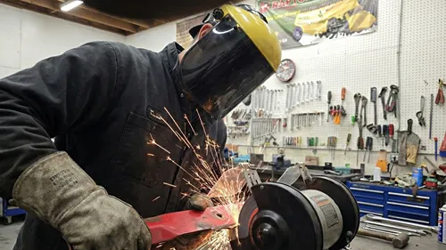 Technician sharpening a mower blade on a bench grinder with sparks flying